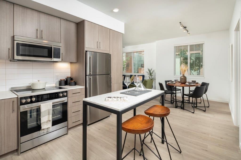 Modern apartment kitchen with gray cabinets, stainless steel appliances, and a dining area.