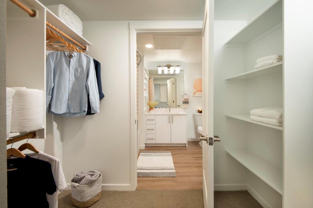 Walk-in closet with hanging clothes, shelves, and a view into a bathroom vanity.