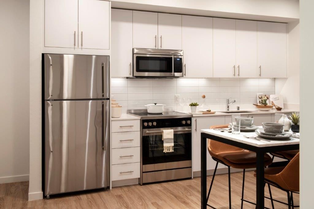Modern apartment kitchen with stainless steel fridge, oven, microwave, and white cabinets.