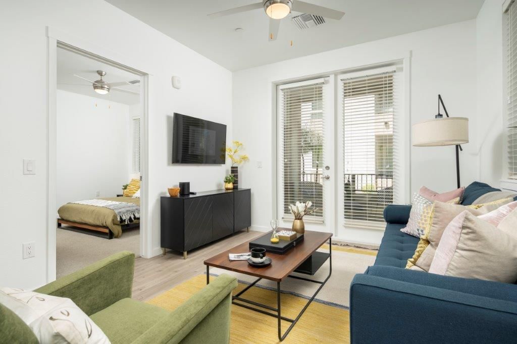 Bright living room in an apartment with blue sofa, green chair, coffee table, and balcony doors.