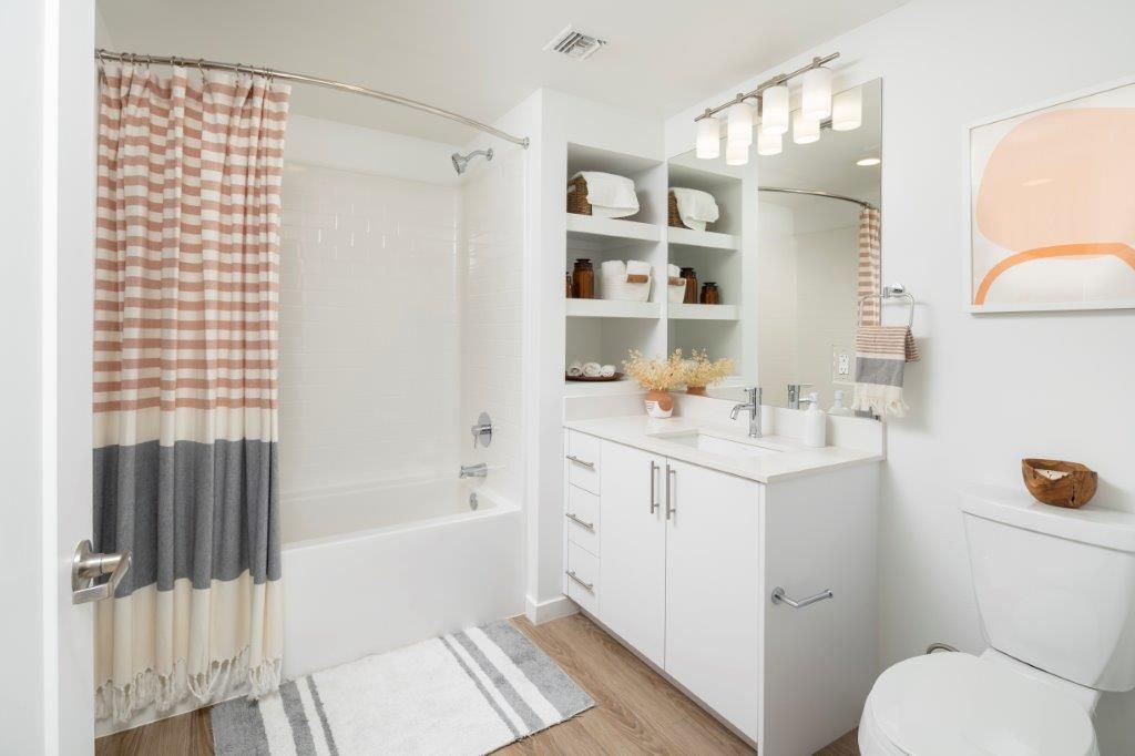 White bathroom with tub/shower, striped curtain, towel shelves, and a white vanity.