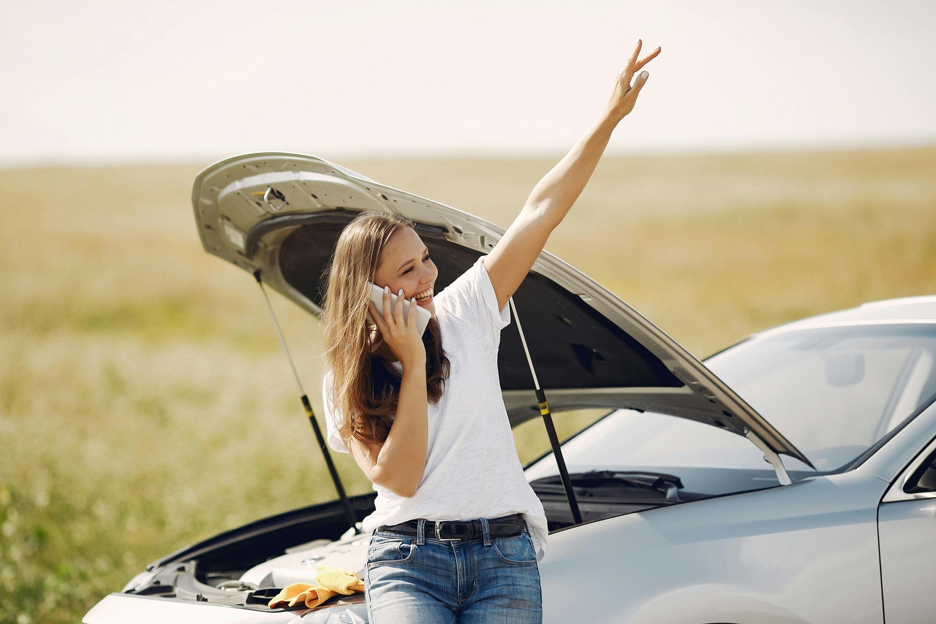 A woman is talking on a cell phone next to a broken down car.