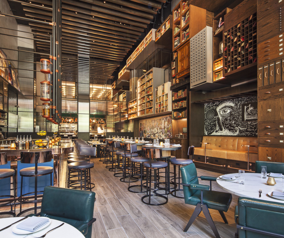 An interior view of a modern, stylish restaurant with dark wood paneling, varied bar and table seating, and ambient light.