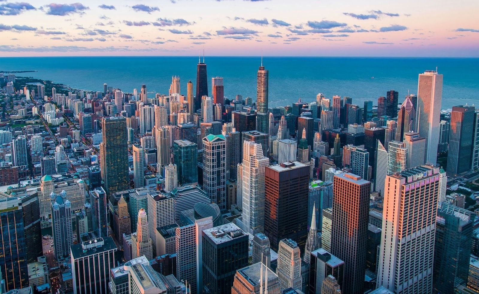 An aerial view of the Chicago skyline featuring skyscrapers along the lakeshore during a colorful sunset.