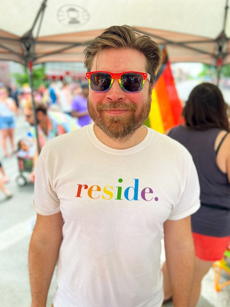 A man wearing sunglasses and a white t-shirt that says reside