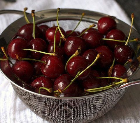 A strainer filled with cherries on a white cloth