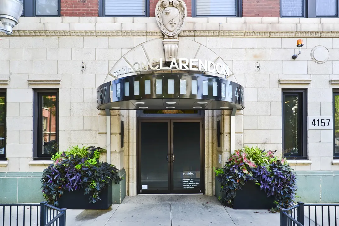 Entrance to the Clarendon apartment building, stone facade with a decorative canopy, potted plants, and the address 