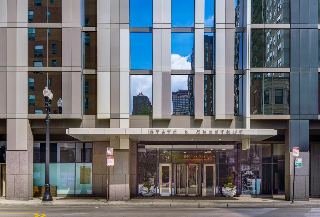 Modern building entrance with glass doors, reflecting sky. 