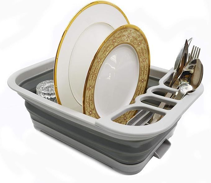A gray, collapsible silicone dish drying rack holding two white decorative plates and several pieces of silverware.