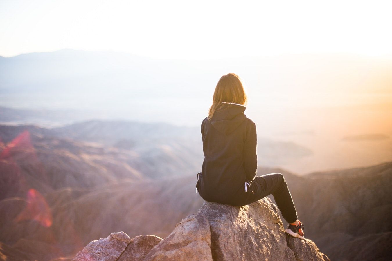 A woman is sitting on top of a mountain looking at the sunset.