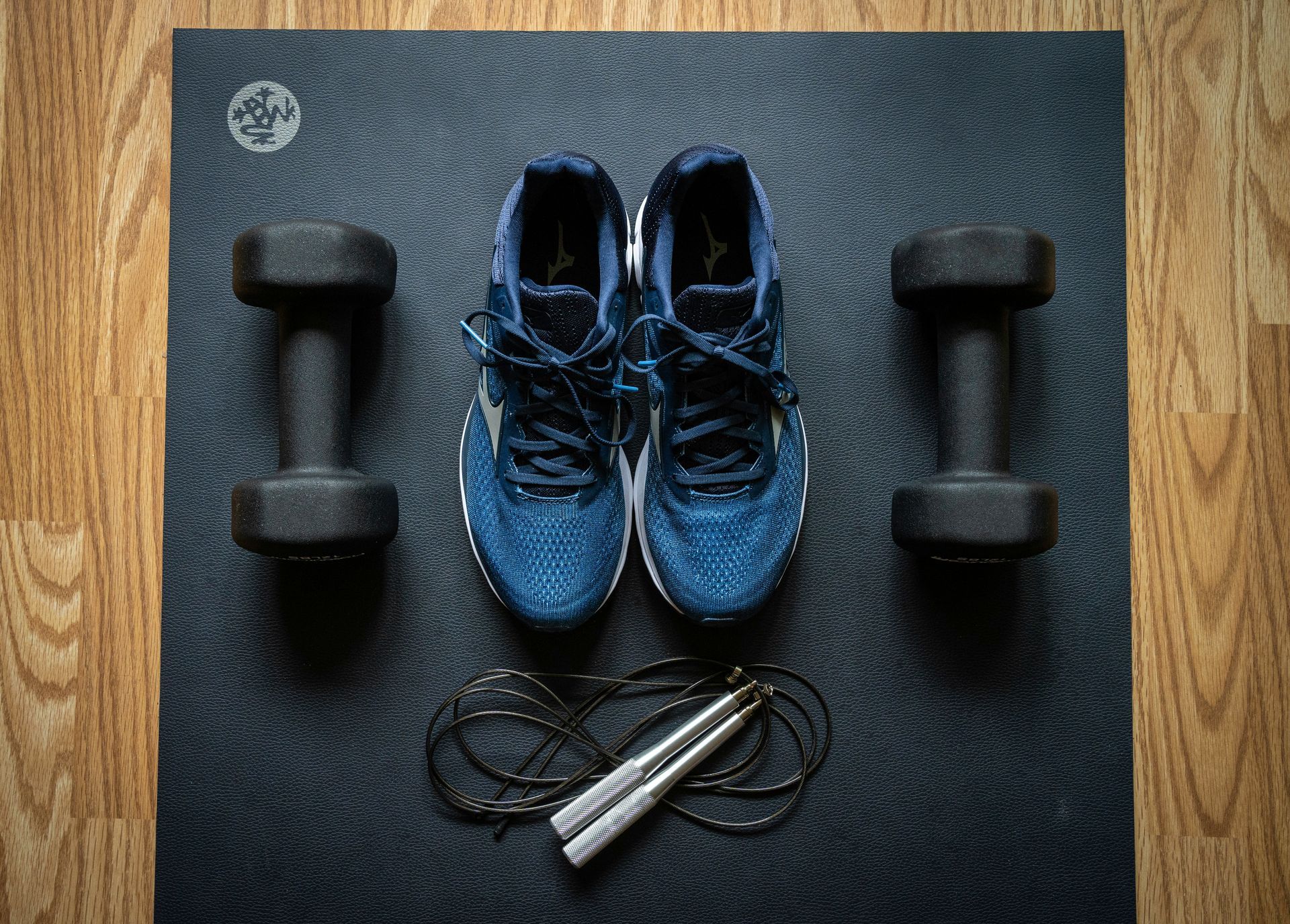 a pair of shoes, dumbbells, and a jump rope are on a mat.