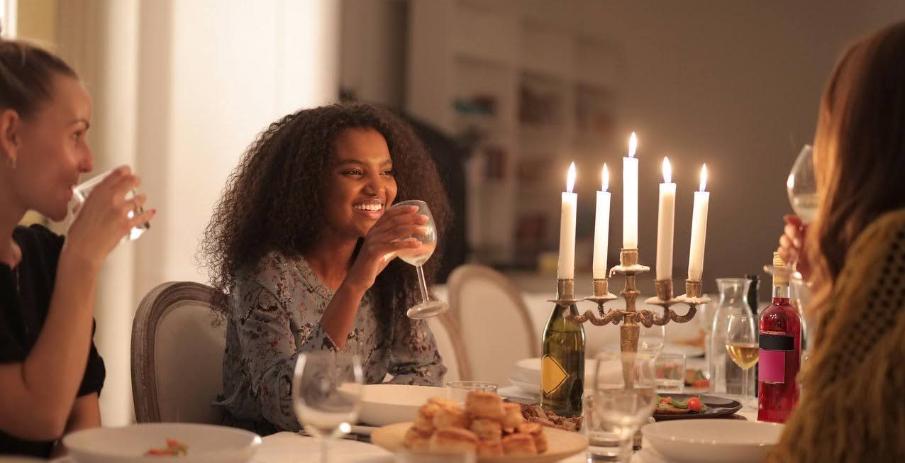 Friends laughing and drinking around a candlelit dining table at home.