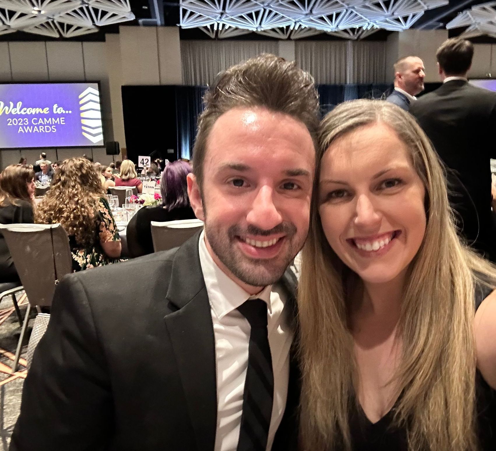 A man and woman are posing for a picture in front of a screen that says welcome to