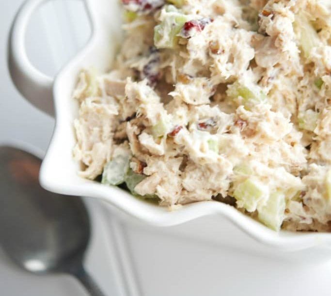 A white bowl filled with chicken salad next to a spoon.