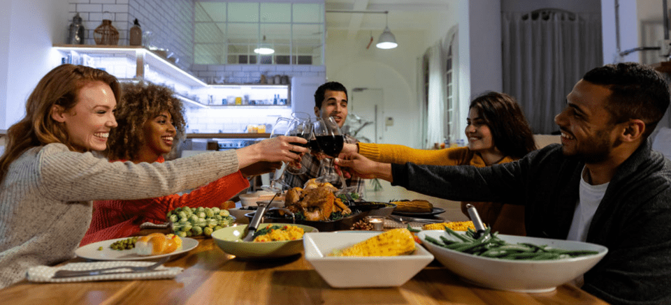Friends share a joyful toast with glasses of wine around a table filled with food in a brightly lit dining room.