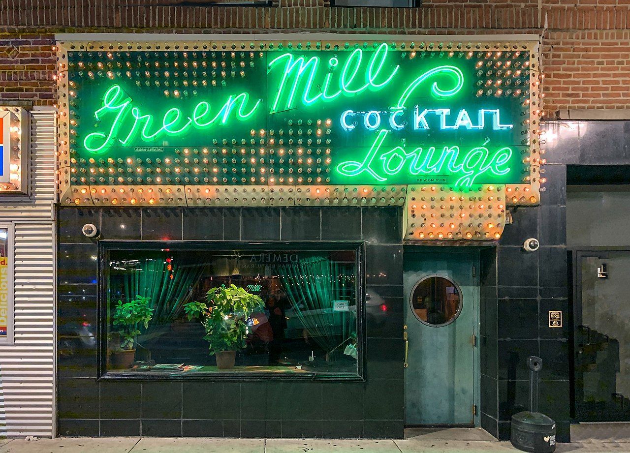 A neon sign for green mill 's cocktail lounge is lit up at night.