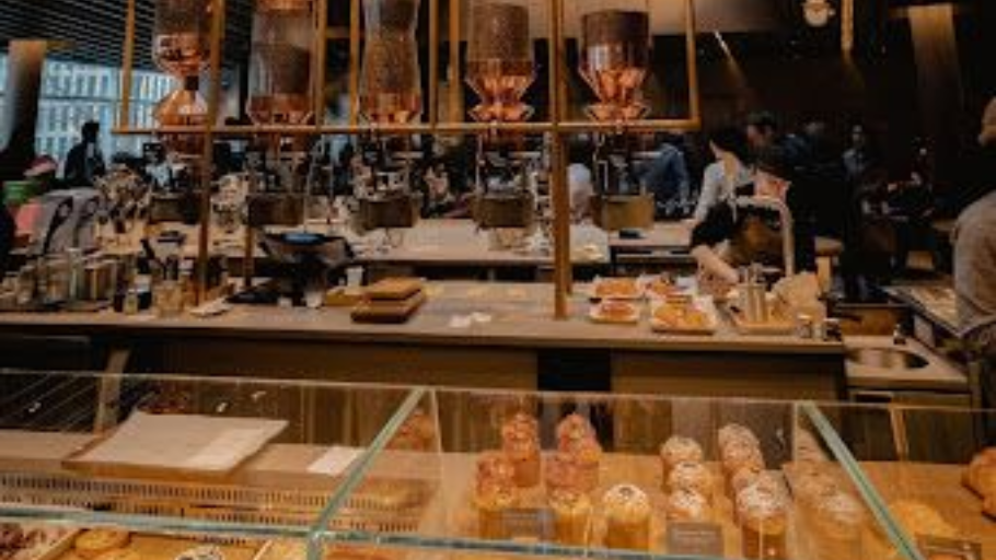 Interior of a modern coffee shop with large copper brewing equipment, glass siphon towers, and pastries displayed on the counter.