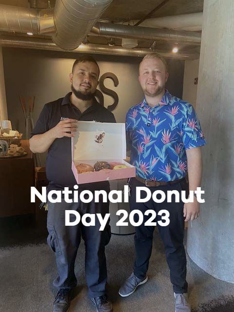 Two men standing next to each other holding a box of donuts for national donut day 2023