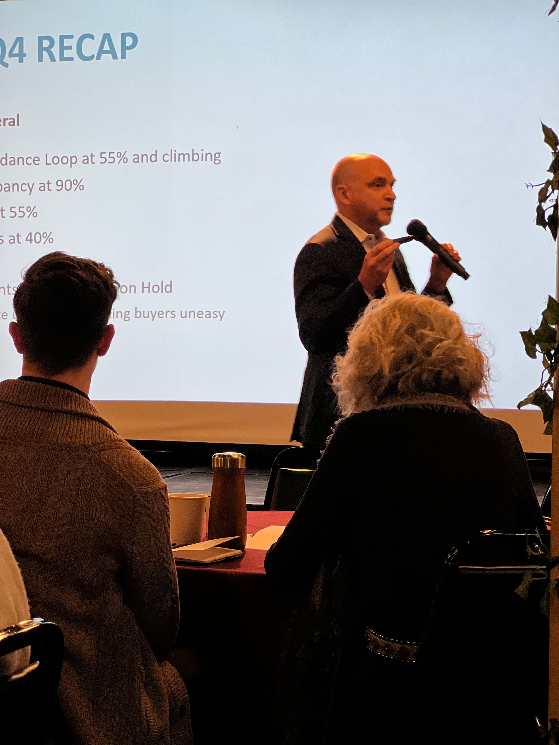 A man is giving a presentation with the word recap on the screen behind him