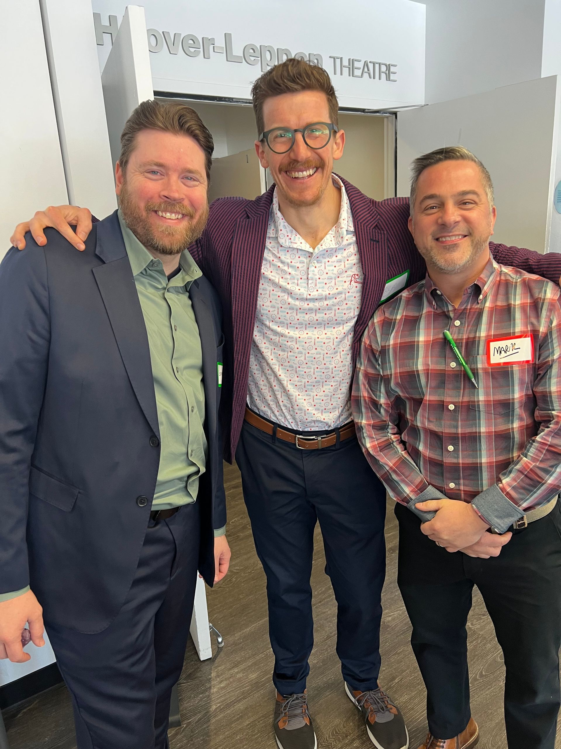 Three men are posing for a picture and one of them has a name tag that says mcv