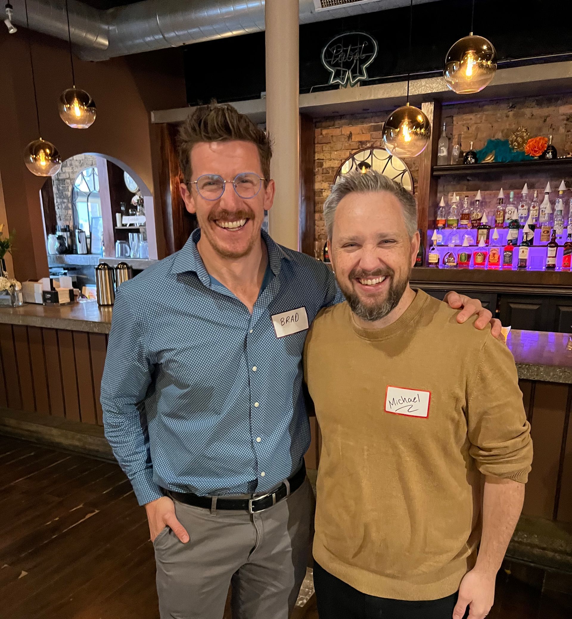 Two men are posing for a picture in front of a bar