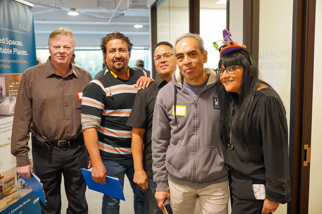 A group of people posing for a picture with one wearing a birthday hat