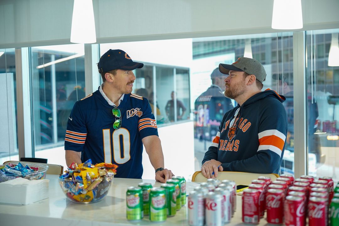 Two men in bears jerseys are standing at a counter talking to each other.