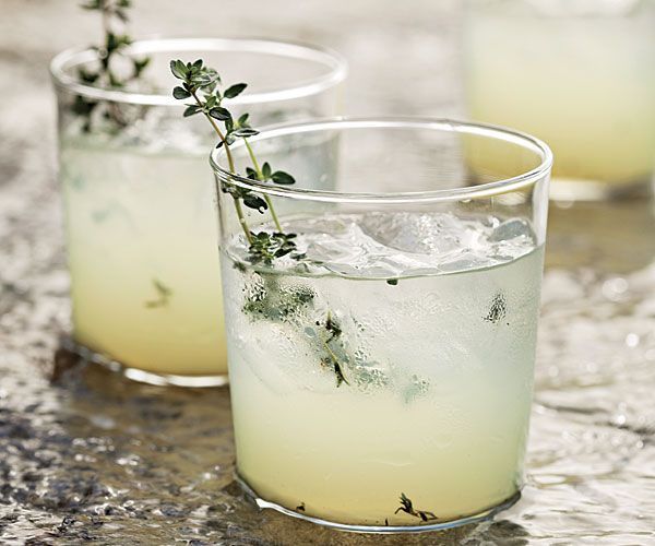 Two glasses of lemonade with ice and thyme on a table.