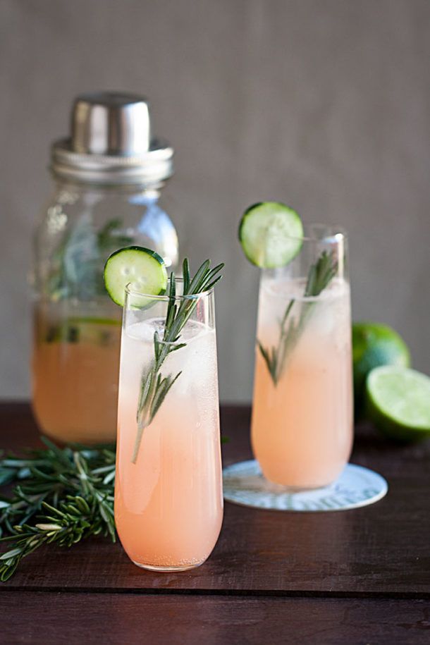 Two glasses of pink drink with cucumber and rosemary on a wooden table.