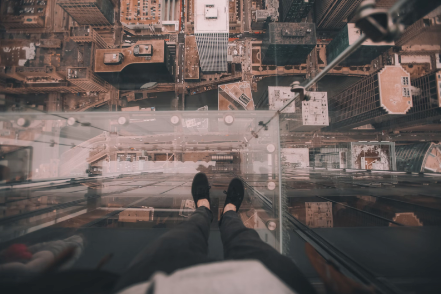 A person is standing on a glass platform overlooking a city.