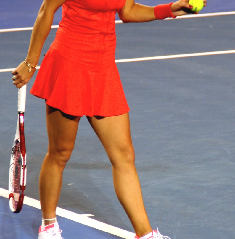 Tennis player in red dress, holding ball and racket on blue court.