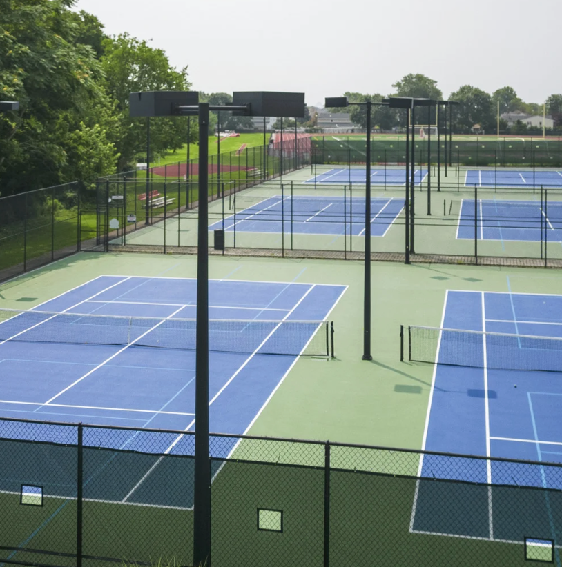 Blue tennis courts with green surrounding areas, black poles, and a black fence.