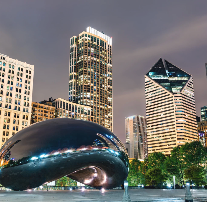 Chicago skyline with the Cloud Gate sculpture (the Bean) in the foreground, at dusk. Skyscrapers in the background.