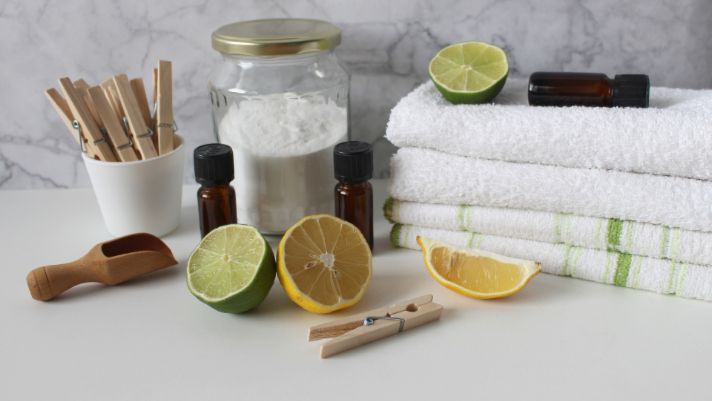 A stack of towels next to a jar of baking soda , lemons , limes and essential oils.