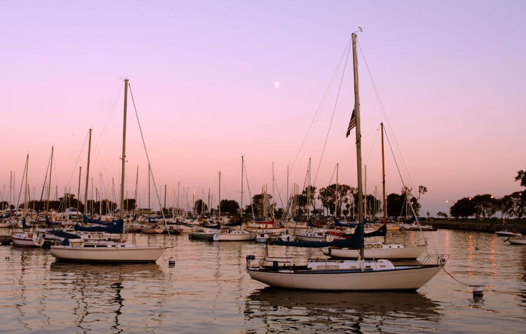A group of sailboats are docked in a harbor at sunset.