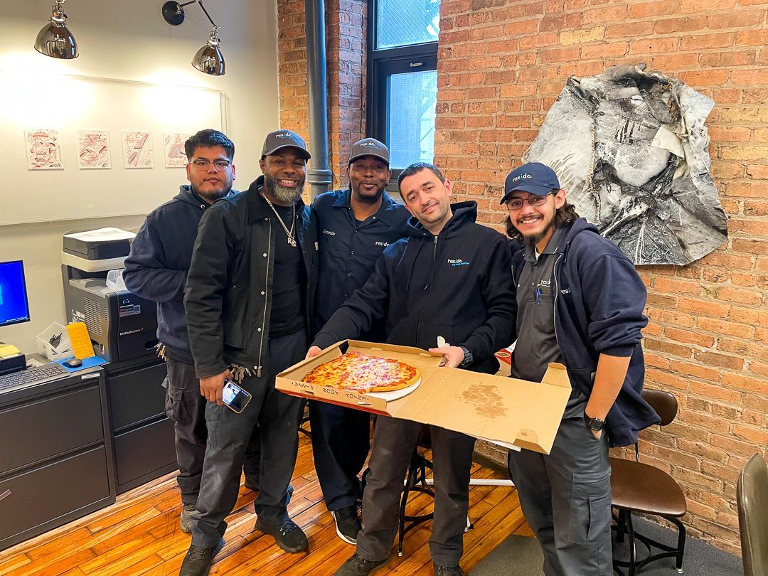 A group of men are standing next to each other holding a pizza box.