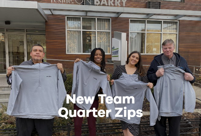 A group of people are holding up sweatshirts in front of a building.