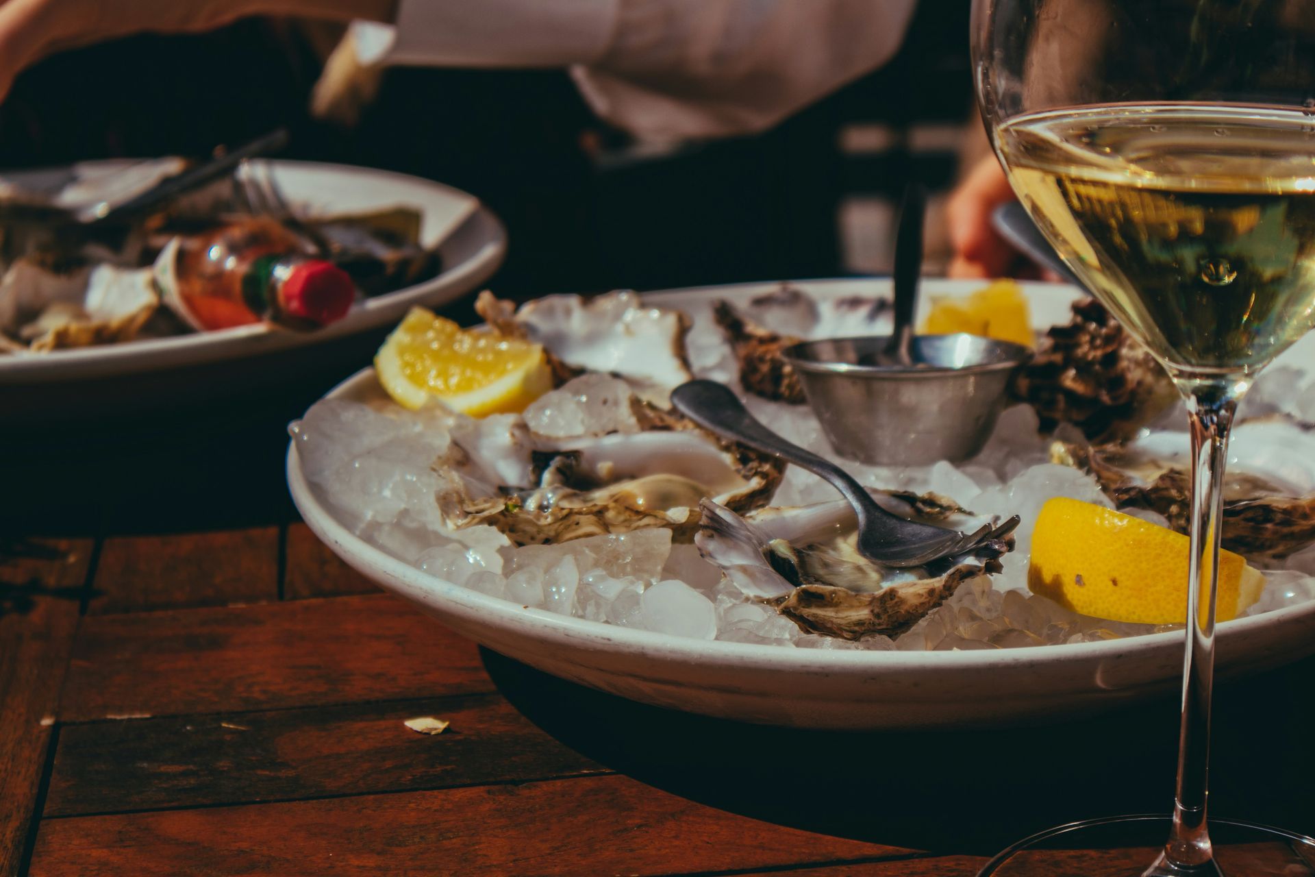 A plate of oysters on ice next to a glass of wine on a wooden table.