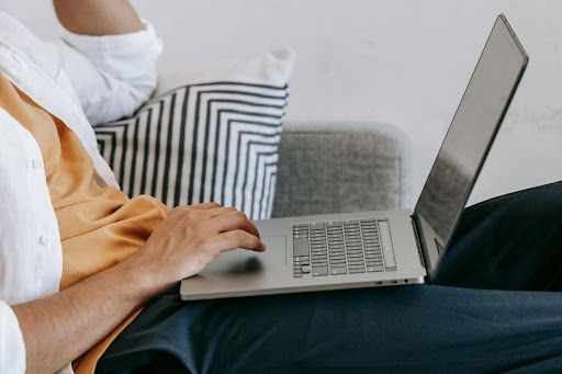 Person using a laptop while sitting on a couch with striped and gray pillows