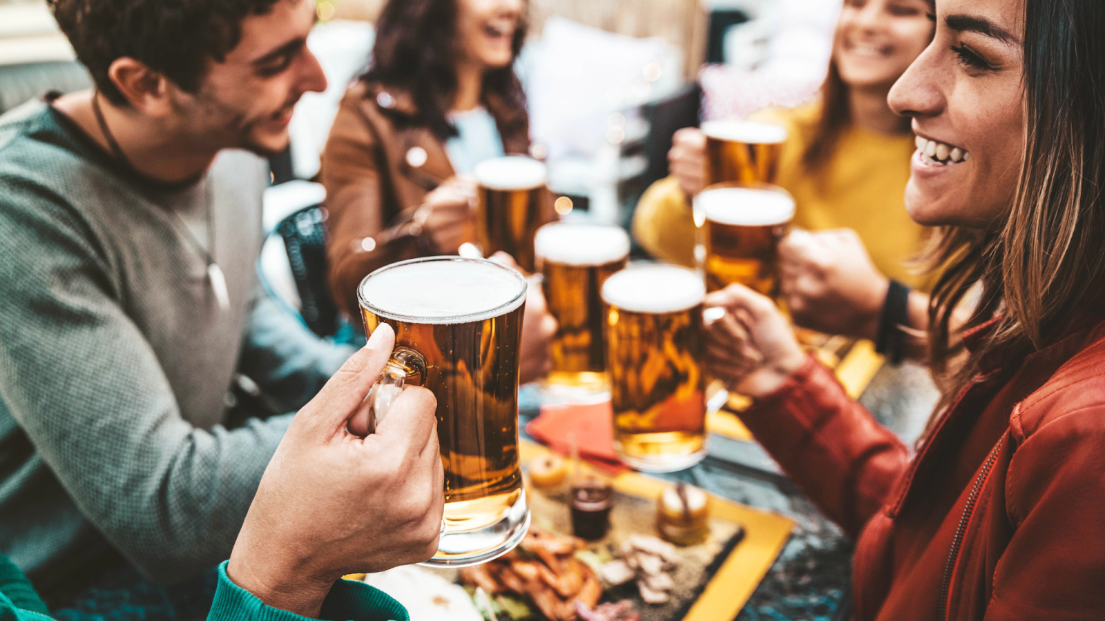 Friends toasting with beer mugs at an outdoor table; smiles and celebration.