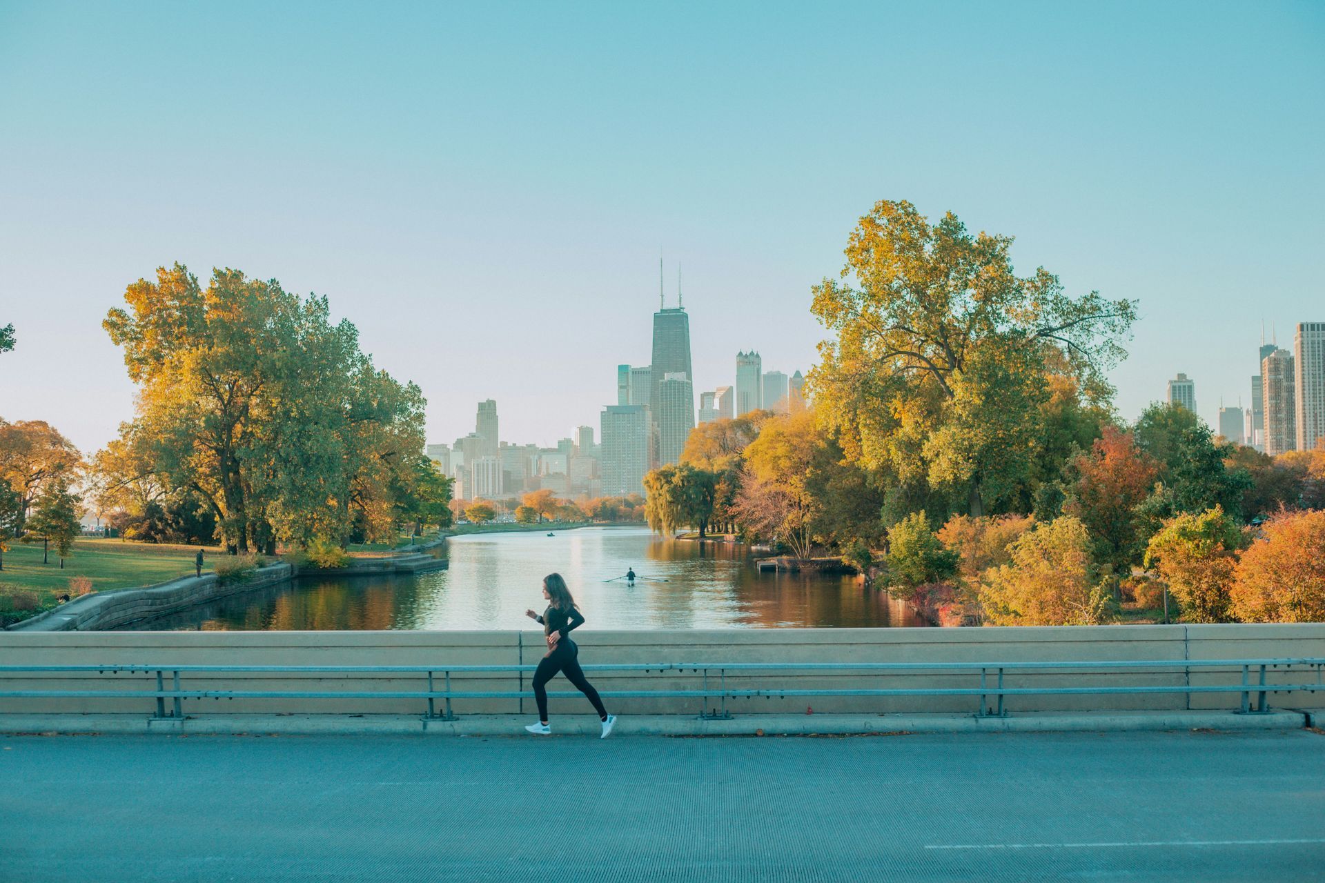 Woman jogging along a waterfront path in Chicago, autumn trees, city skyline in the background.