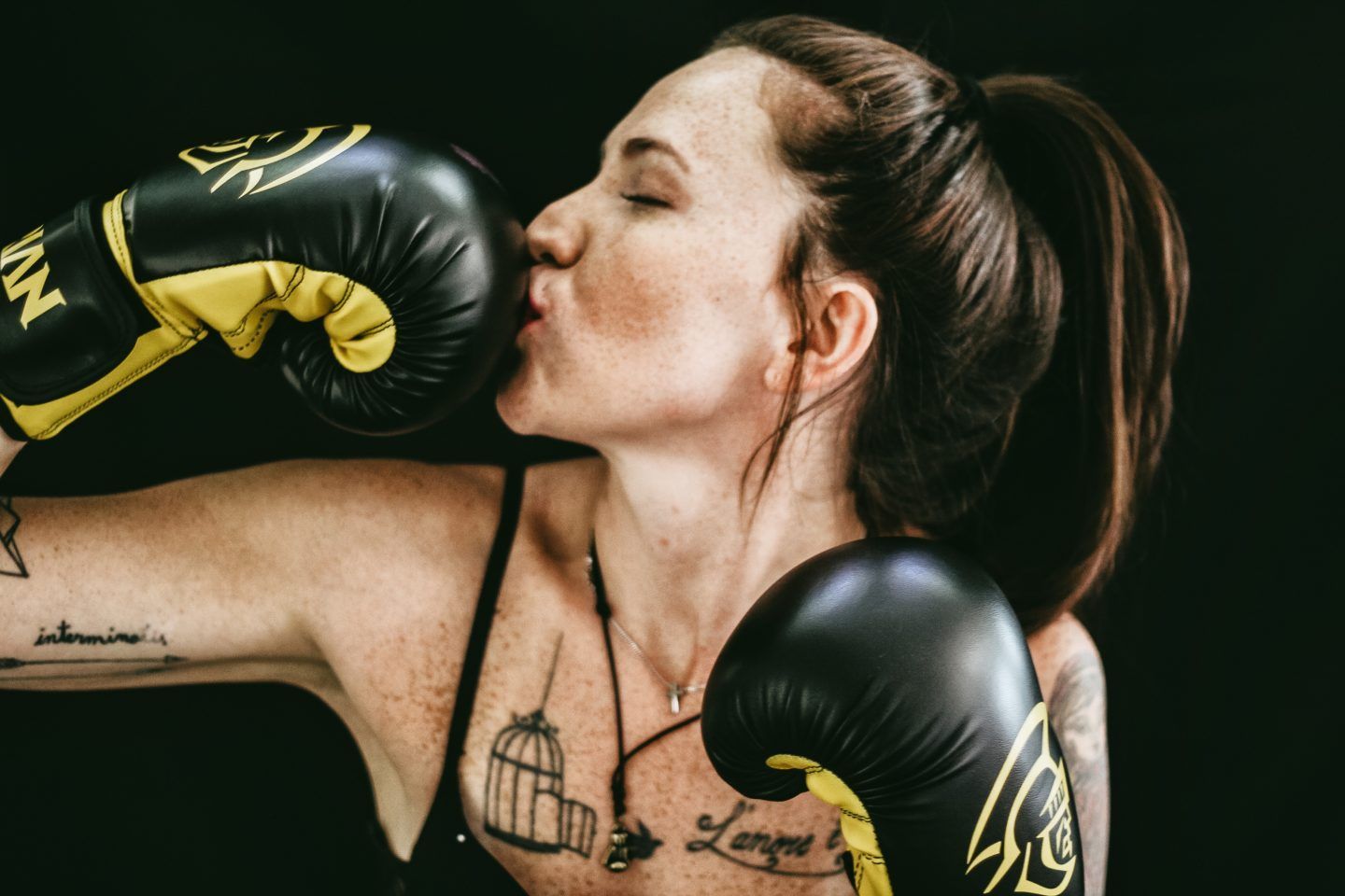 A woman is kissing a pair of boxing gloves.