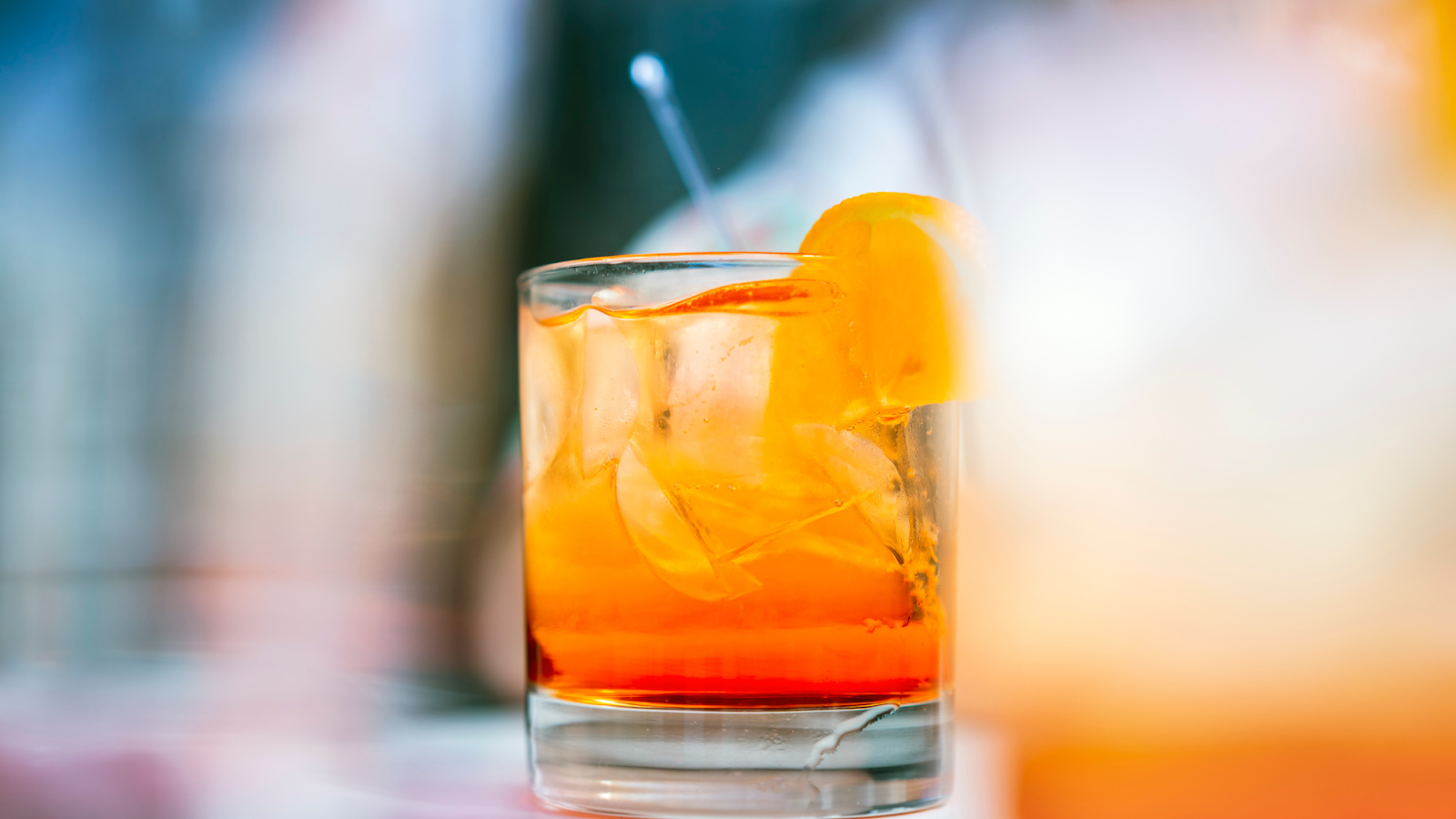 Orange cocktail in a glass with ice and a lemon wedge garnish.