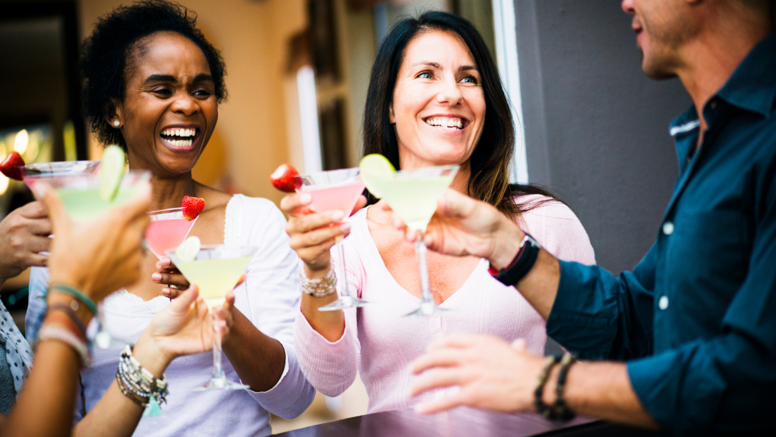 People toasting cocktails, laughing, outdoors.