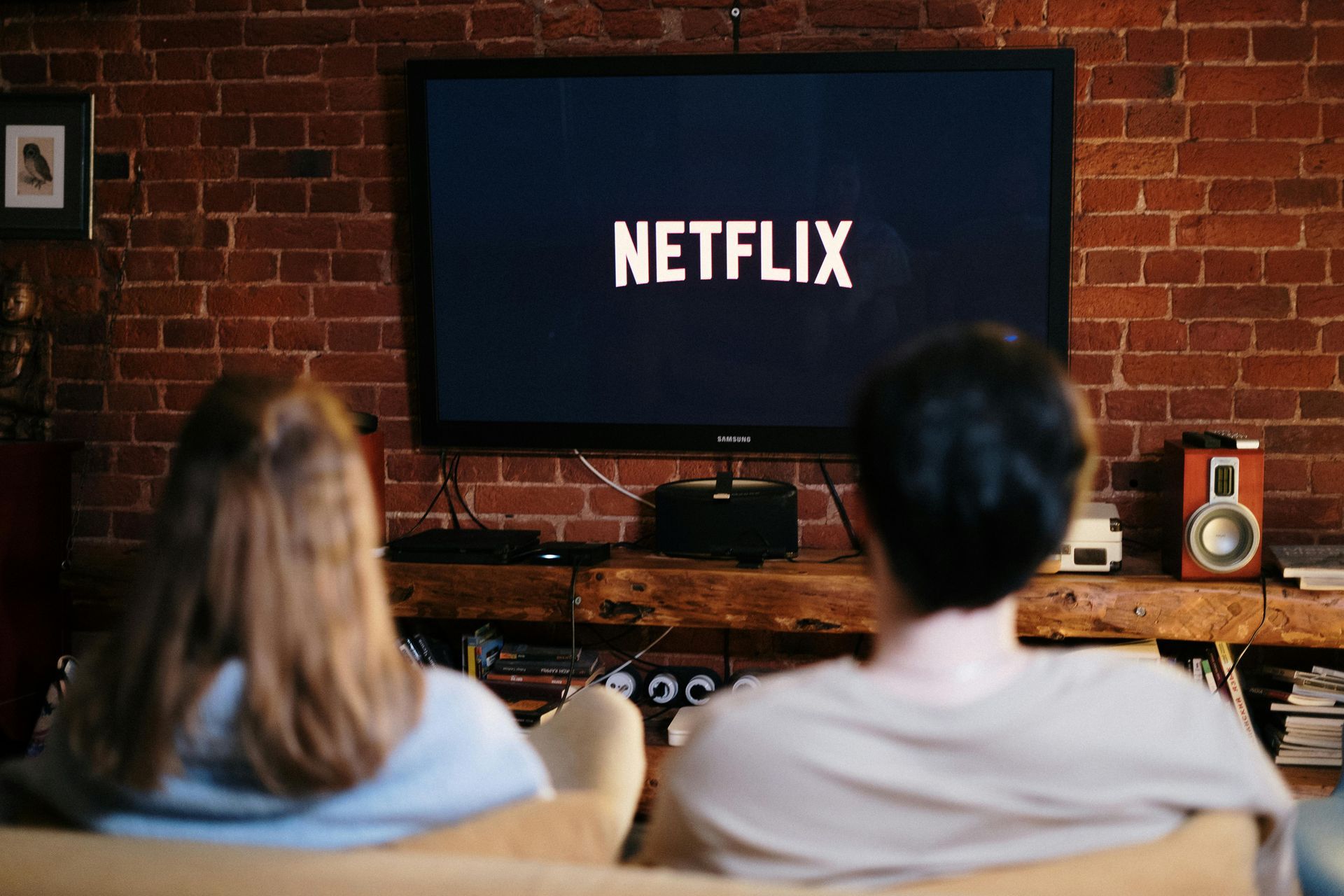 A man and a woman are sitting on a couch watching netflix on a television.