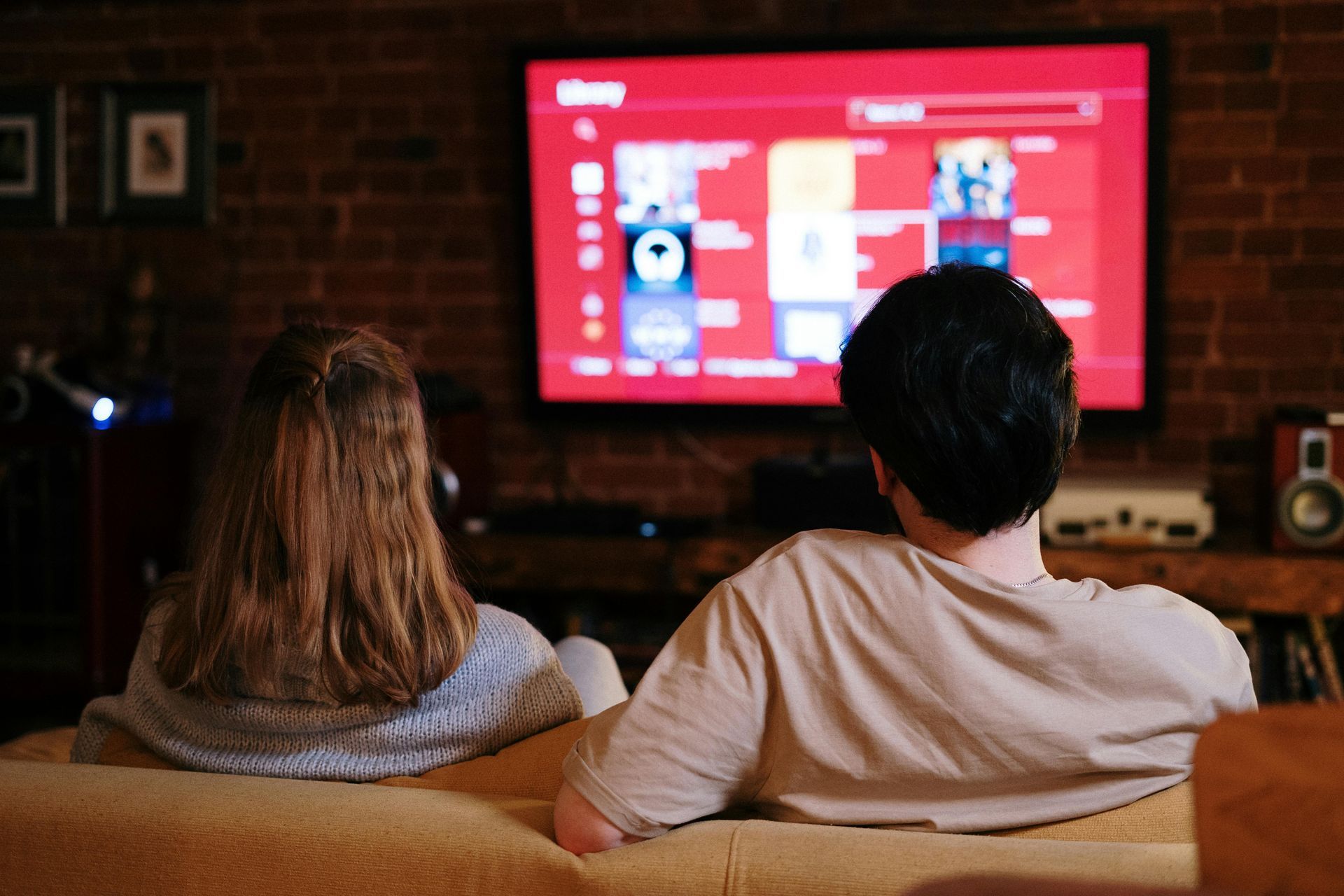 A man and a woman are sitting on a couch watching a television.