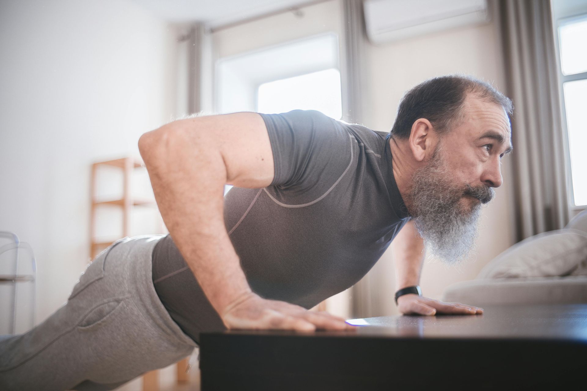 A person performing an incline push-up against a dark table in a brightly lit room.