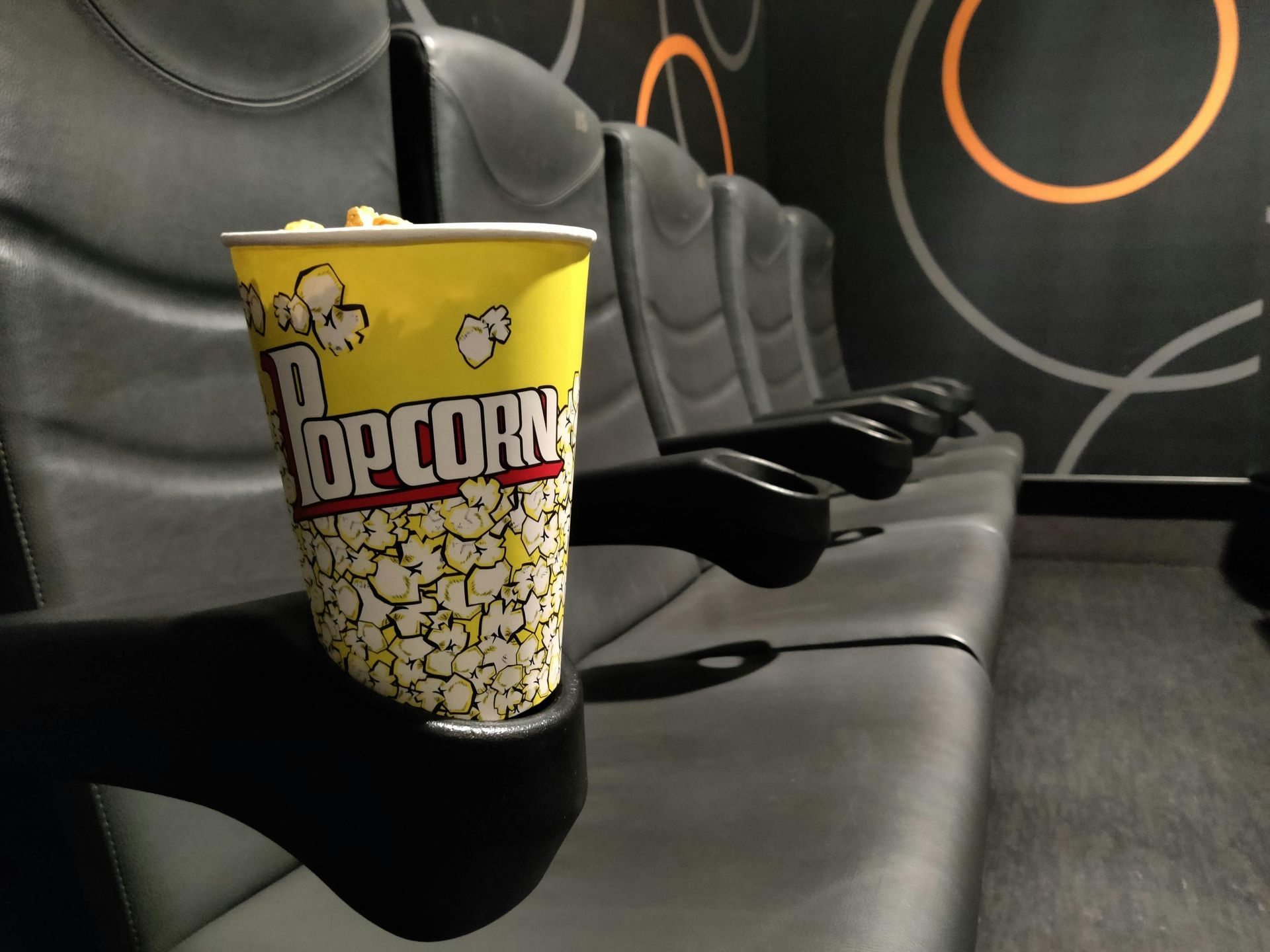 A cup of popcorn sits on a chair in a movie theater