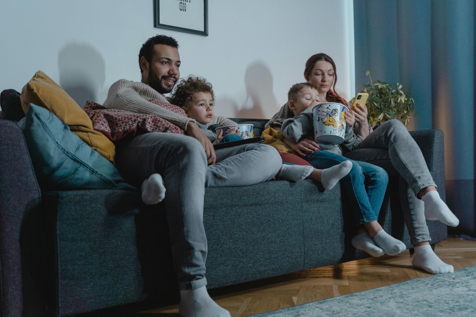 A family is sitting on a couch watching tv and eating popcorn.