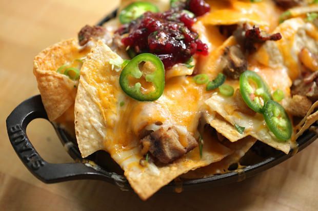A bowl of nachos with cheese , jalapenos and cranberry sauce on a wooden table.